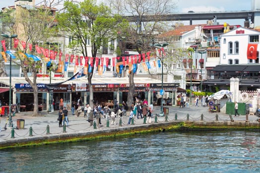 Istanbul, Turkey - May 8 2023: Ortakoy Square, a popular tourist destination by the Bosphorus Strait with pedestrians walking around and taking memorial photos. Bosphorus bridge appears in the far end