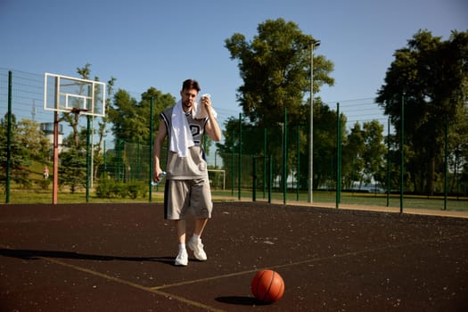 Tired sweaty basketball player with tower on shoulders over urban street court. After training