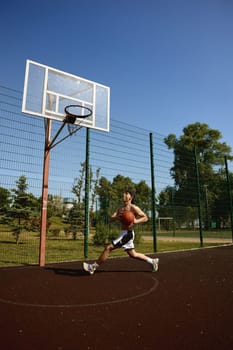Shot in motion of teenager basketball player running with ball on street sports court. Everyday sports activity outdoors
