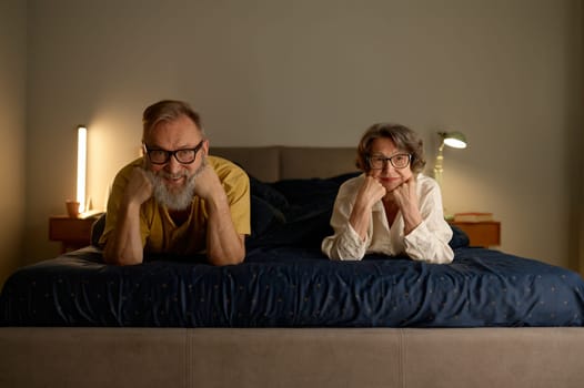 Portrait of smiling senior family couple in bed looking at camera. Happy retirement and best relationship