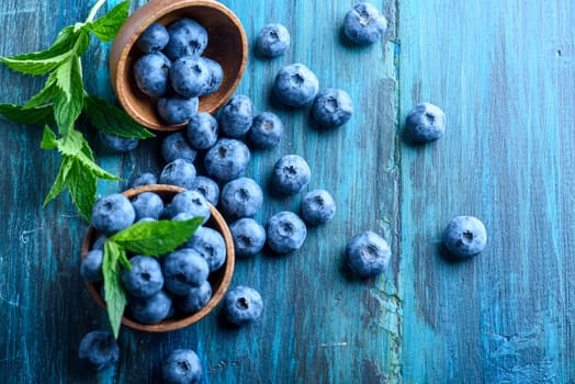 Bowl of fresh blueberries on blue rustic wooden table from above. Top view of healthy organic seasonal fruit pattern background. Organic food blueberries and mint leaf overhead for healthy lifestyle.