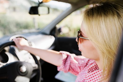 Young blond woman with sunglasses driving car. Casual hipster girl driver travel in vehicle.