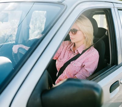 Young blond woman driving a car. Casual girl with sunglasses traveling in vehicle.
