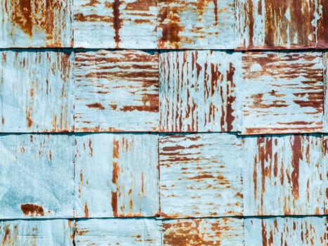 Frame-filling close-up view of overlapping square light blue metal plates with rusty spots.