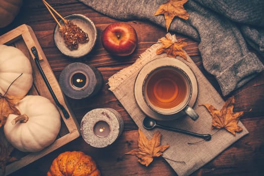 Autumn mood concept. Warm, cozy and rustic still life with cup of tea, candle and pumpkins.