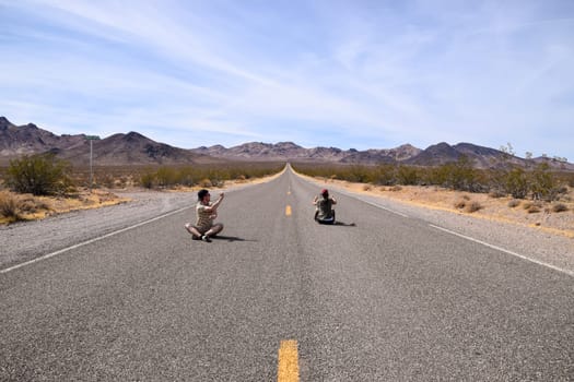 Two people pretending to drive on a highway in the Death Valley, USA