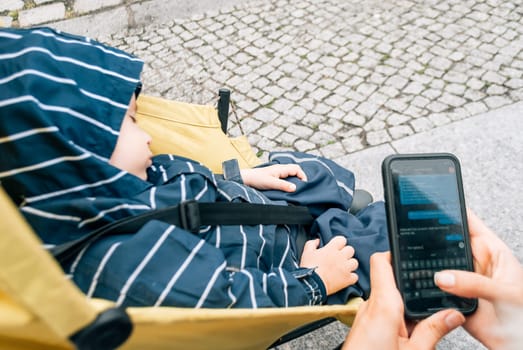 A woman corresponds via text messages in a messenger near a stroller with a small child.