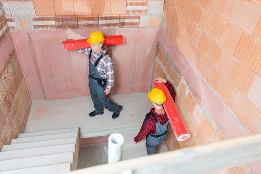 Overhead view of two male construction worker carrying red pipes on their shoulder walking staircase
