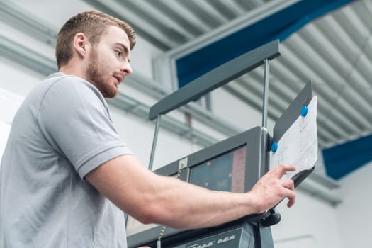 Worker in the metal industry entering data on screen of a modern machine tool in factory