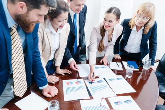 Multi-ethnic team of five dedicated specialists smiling while analyzing various charts with positive statistics about the profit and the development of the company