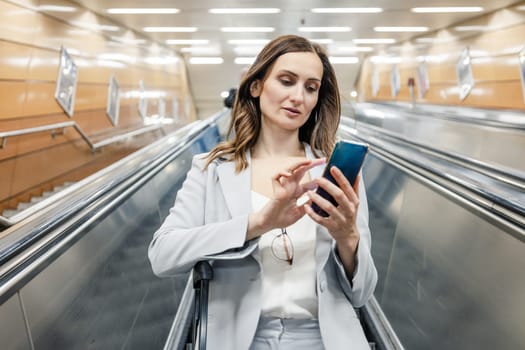 woman in suit going down an escalator to the subway station looking at her phone
