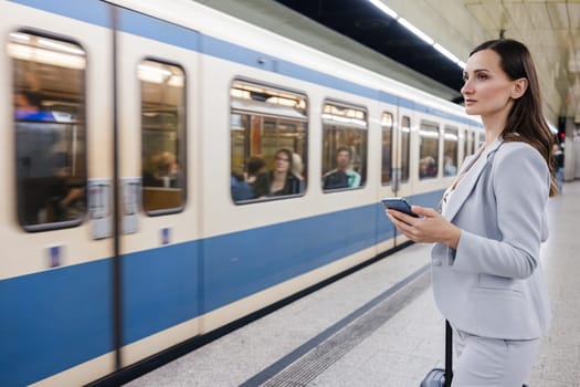 woman in suit with phone in her hand in subway station with train arriving