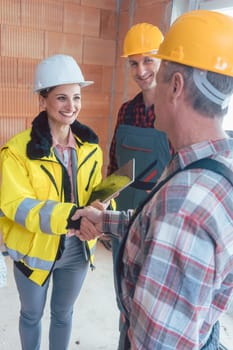 Smiling female contractor with tablet computer shaking hand of senior builder before starting work