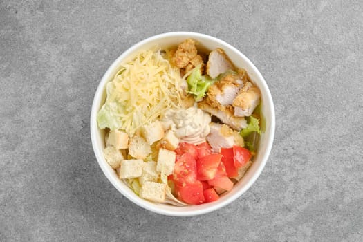 Top view of salad with chicken meat, cheese, tomatoes, iceberg lettuce and crouton in cardboard bowl