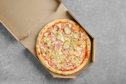 Top view of pizza with ham and pickled cucumber in takeaway cardboard box
