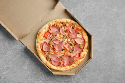 Top view of pizza with ham, sausage, olives and bell pepper in cardboard box
