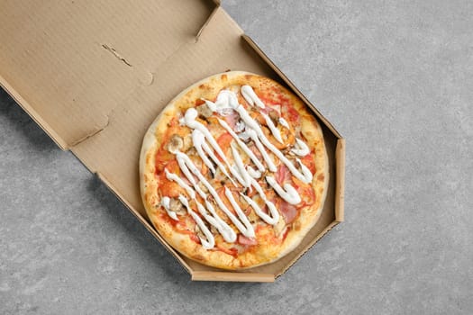 Top view of pizza with ham, champignon and tomato slices covered with mayonnaise in cardboard box