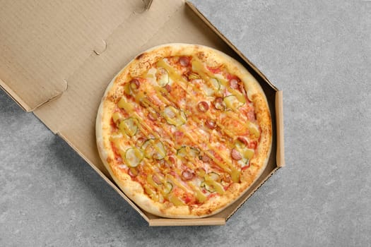 Top view of pizza with thin sausage and pickled cucumber in cardboard box