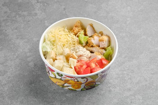 Salad with chicken meat, cheese, tomatoes, iceberg lettuce and crouton in cardboard bowl