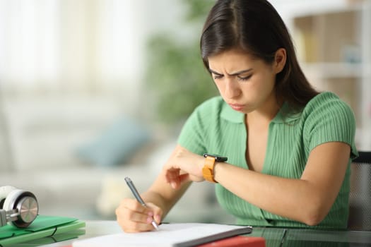 Frustated student checking smartwatch studying at home