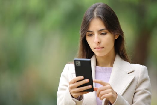 Serious woman using phone in winter outside walking in a park