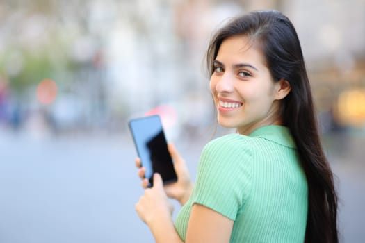 Happy woman twirling using cell phone walking in the street looking at camera