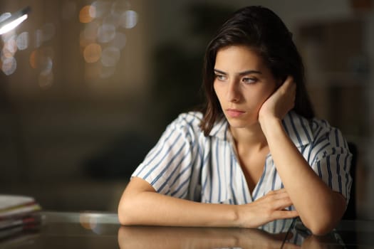 Sad pensive woman looking away alone at home in the night
