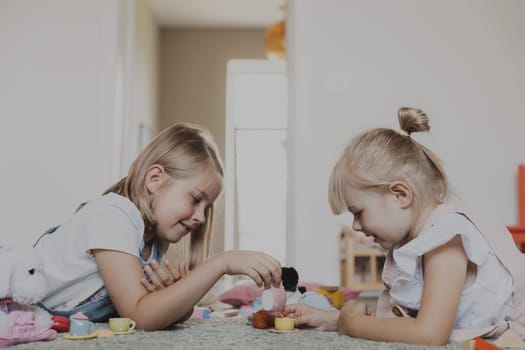 Close-up of female children playing with colorful toy play tea set. Kids lying at home bedroom or kindergarten, nursery. Educational eco-friendly game for child. Development of logical thinking