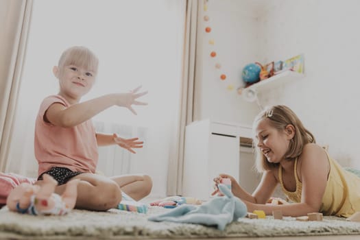 Children playing with colorful toys. Kids sitting on carpet at home bedroom or kindergarten, nursery. Educational eco-friendly game for child. Cute little sisters build house, tower, having fun