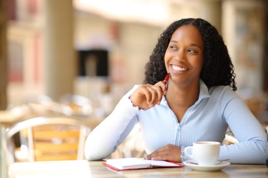 Happy black woman with agenda thinking looking at side in a bar terrace