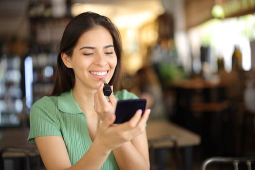 Happy woman painting lips sitting in a restaurant waiting in a date