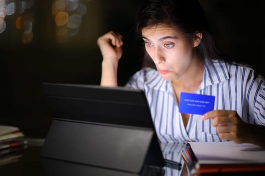 Perplexed student buying online with credit card and laptop in the night at home or office