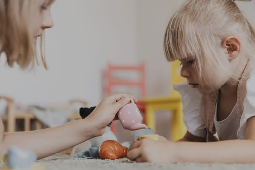 Close-up of female children playing with colorful toy kitchen play tea set. Kids lying on carpet at home bedroom, kindergarten. Educational eco-friendly games. Development of motor skills, imagination