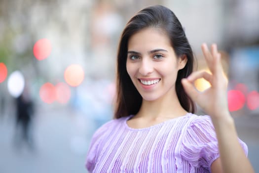 Happy woman gesturing ok standing in the street looking at you