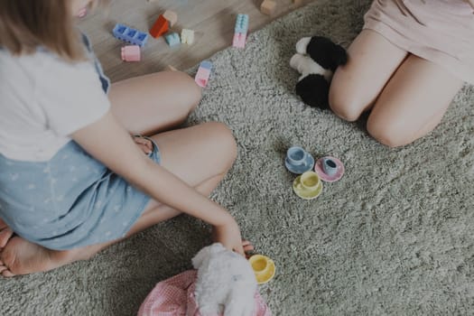 Children playing tea party with colorful ceramic kitchen set. Kids sitting on carpet at home bedroom, kindergarten, daycare playroom, playground, play center. Educational eco-friendly child games