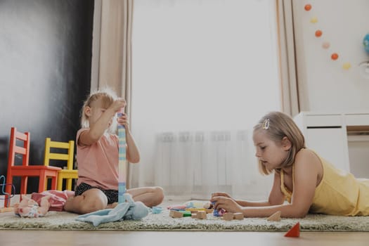 Children playing with colorful wooden toy train. Kids sitting on carpet at home bedroom, kindergarten, daycare playroom, playground, play center. Funny educational eco-friendly game for child