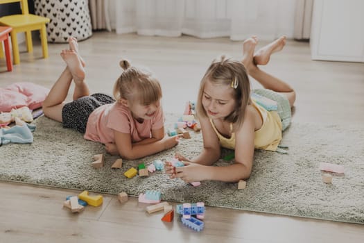 Children playing with colorful toys. Kids lying on carpet at home bedroom or kindergarten, nursery. Educational eco-friendly game for child. Playtime leisure activity, enjoying family bonding time