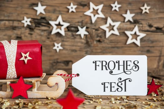 Wooden Sled With Red Gift And Rustic Christmas Background With Label With German Text Frohes Fest, Which Means Happy Holidays In English