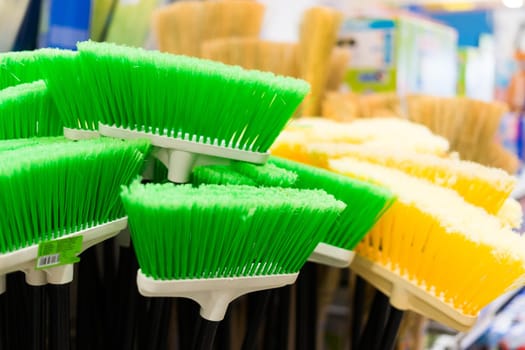 Plastic brushes for cleaning premises. Assortment of multi-colored brooms in store. Close-up
