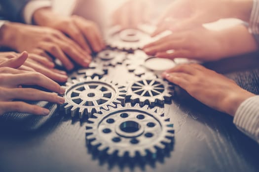 People joining cog wheel on the black desk. Concept of the teamwork, partnership and cooperation.