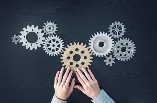 Man hands putting a cogwheel into a common mechanism. Abstract background. Concept of the own business and partnership.