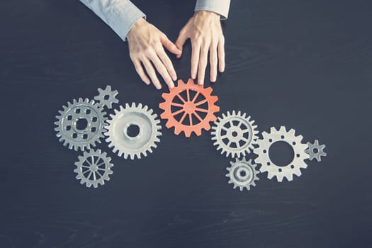Man hands putting a cogwheel into a common mechanism. Abstract background. Concept of the own business and partnership.