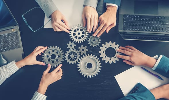 People joining cog wheel on the black desk. Concept of the teamwork, partnership and cooperation.