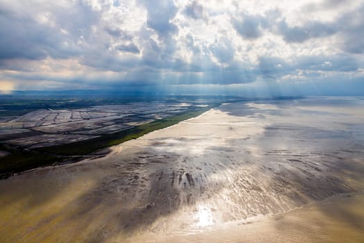A wide-angle shot of the sun shining through clouds onto the land and sea beach. represents the power of nature. The sun is the power of life. The light from the sun nourishes all living things.