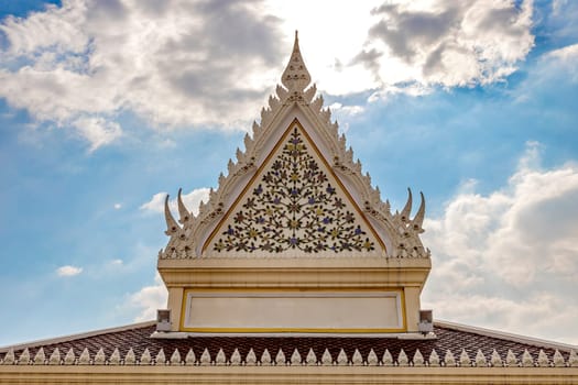 Gables with beautiful patterns on the roof of temple in Thailand during the day. There is blue sky and clouds in the background. Sunlight shines from behind the clouds. There is space to put the name.