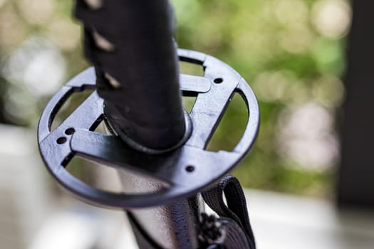 A shallow focus shot of Tsuba, or hand guard, on the handle of a katana (Japanese long sword) It is a work of art that is widely popular and has a high price. The background is a blurred fence line.