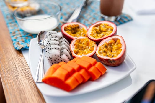 A shallow focus shot of a white plate of fruit at breakfast in a hotel. Dragon fruit, papaya. The background is a bowl of finished milk.