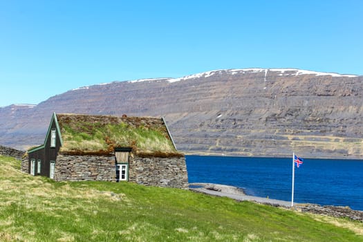 Icelandic flag in front of a romantic turf house, Iceland