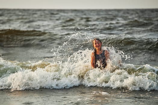 Little girl playing with waves in the sea. Kid playfully splashing with waves. Child jumping in sea waves. Summer vacation on the beach. Water splashes. Travel during summertime concept