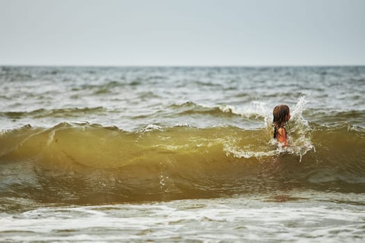 Little girl playing with waves in the sea. Kid playfully splashing in waves. Child jumping in sea. Vacations on the beach. Water splashes. Fun and play during summer vacation. Travel concept